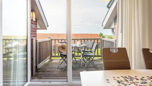 Een balkon met een tafel en stoelen, een hanglamp en uitzicht op een bakstenen gebouw.
