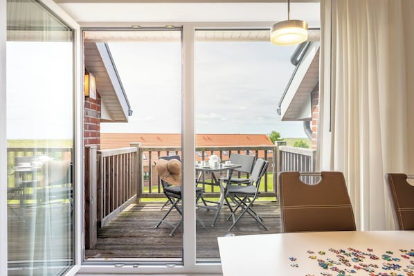 A balcony with a table and chairs, a hanging light fixture, and a view of a brick building. - Bright vacation apartment at Wremer Bogen 9-3-3 with a view of the seawall. (Wurster Nordseeküste)