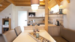 A modern kitchen with wooden beams, a dining area with a table set for two, and a cozy seating area. - Vacation home Philipp. Between sea and marshland. (Wurster Nordseeküste)