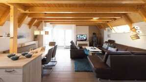 A spacious living area with a wooden ceiling, a sofa, a coffee table, and a television. - Vacation home Philipp. Between sea and marshland. (Wurster Nordseeküste)
