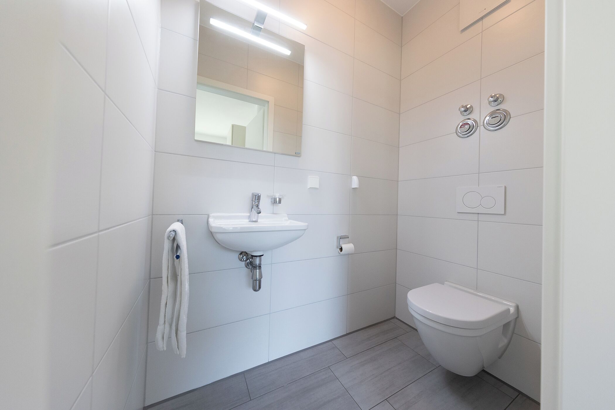 A modern bathroom with a white sink, mirror, and toilet.
