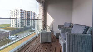 Ein Balkon mit Korbmöbeln, einem Tisch mit Weingläsern und Blick auf ein Gebäude gegenüber.