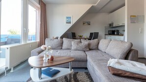 Ein modernes Wohnzimmer mit einem Ecksofa, einem Holztisch und Blick auf den Balkon.