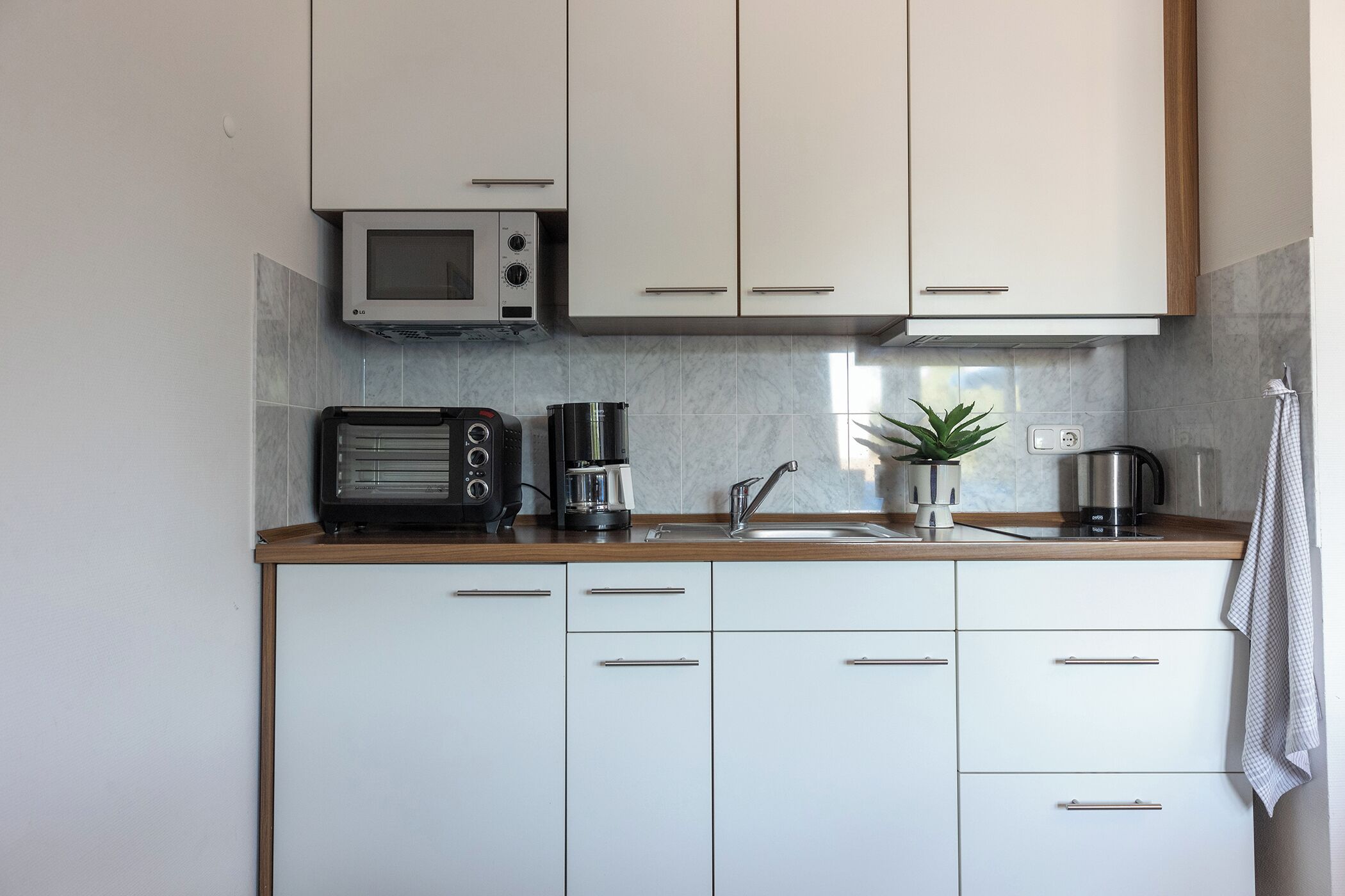 A modern kitchen with white cabinets, a microwave, a toaster, and a coffee maker.