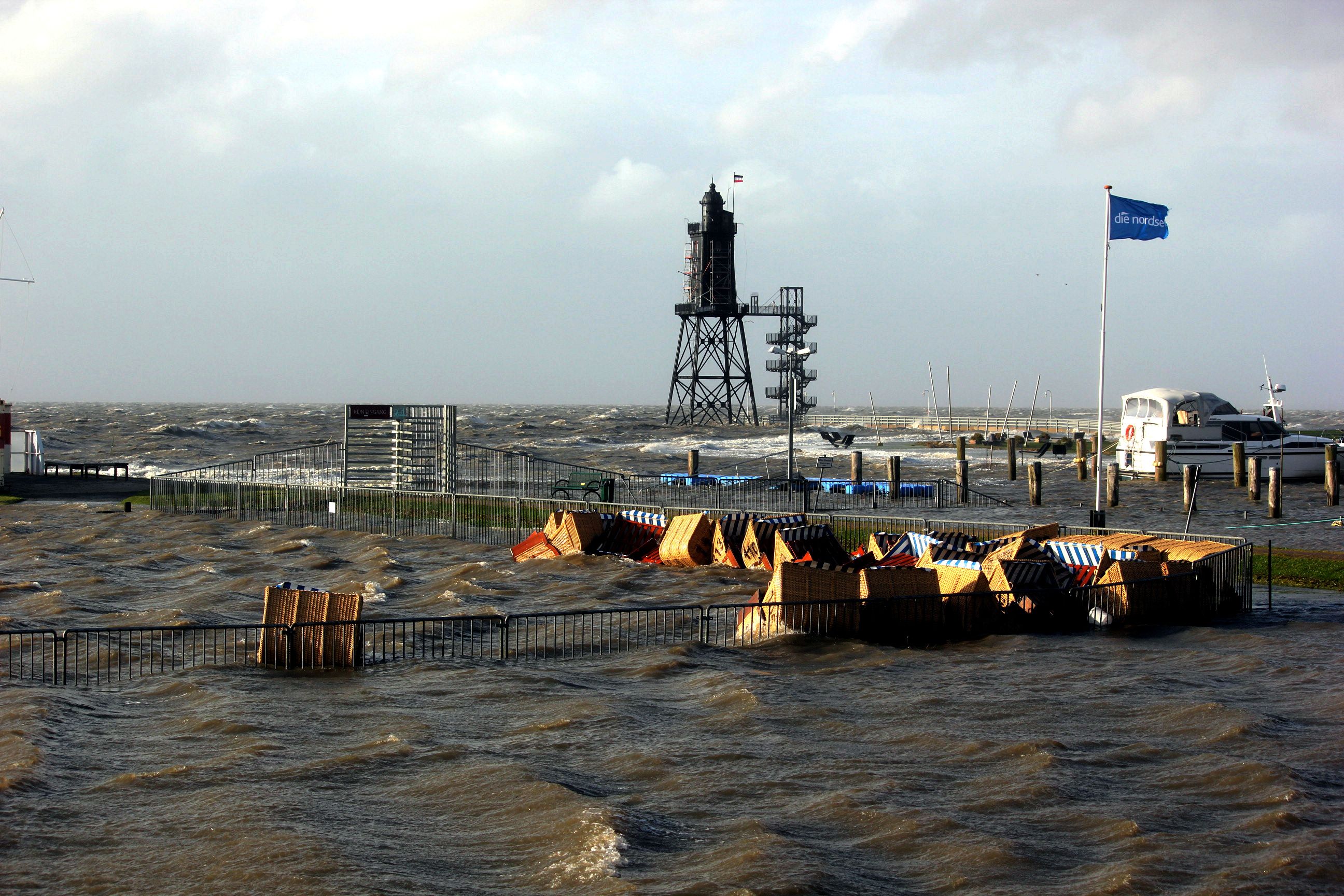A coastal area with a lighthouse, a pier, and a flag.