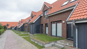 Une rangée de maisons modernes en briques, avec des toits recouverts de tuiles rouges, des volets gris et un trottoir dallé.