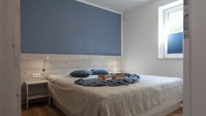 A bedroom with a bed, a nightstand, a window, and a blue wall.