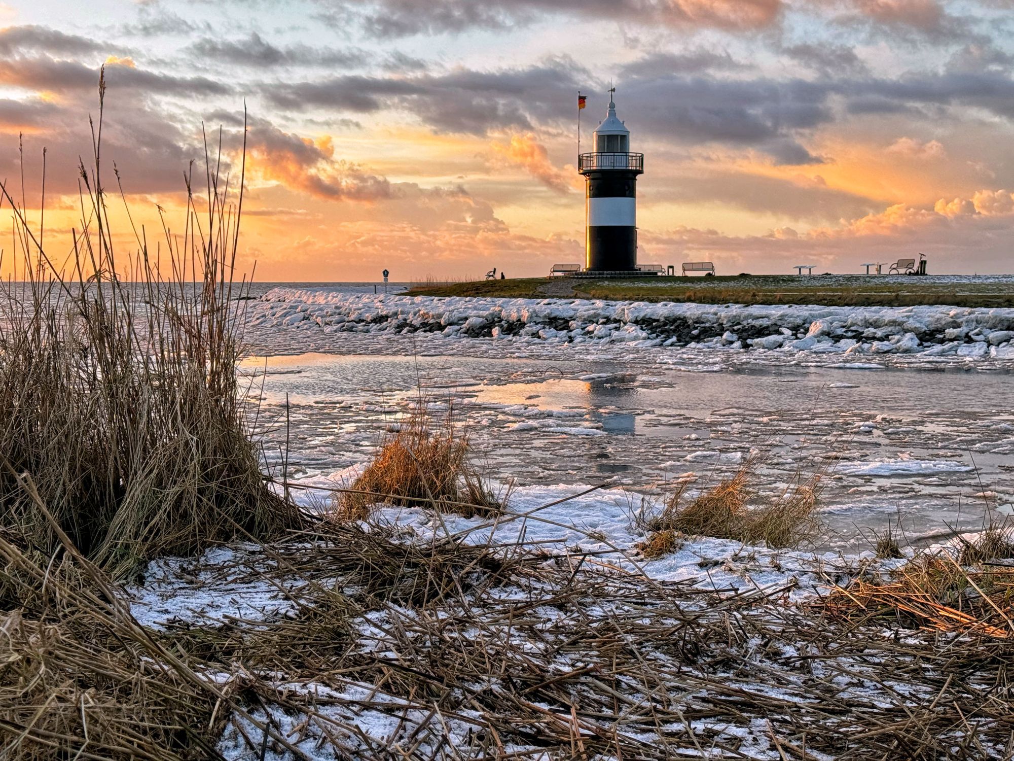 Un phare sur une côte rocheuse, entouré de neige et de glace, sous un ciel nuageux.
