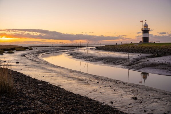 A coastal landscape with a lighthouse, calm water, and a clear sky.