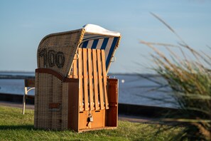Ein Strandstuhl mit Streifenmuster und einem Korbwäschekorb, platziert auf Rasen in der Nähe eines Gewässers.