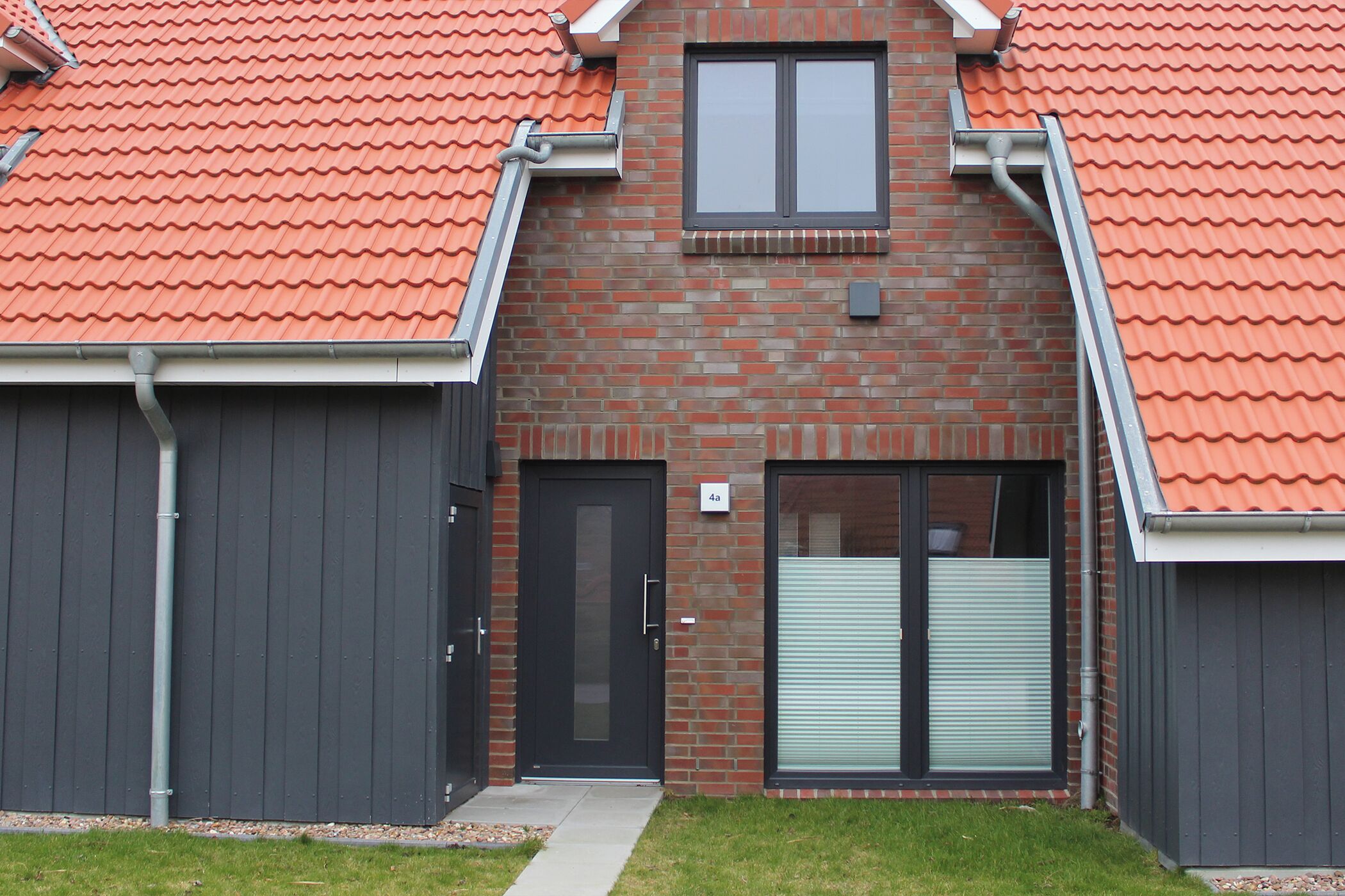Een modern gebouw met een gevel van baksteen, twee grote garagepoorten en een klein raam.