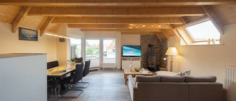 A modern living room with a wooden ceiling, a sofa, a dining table, and a TV.