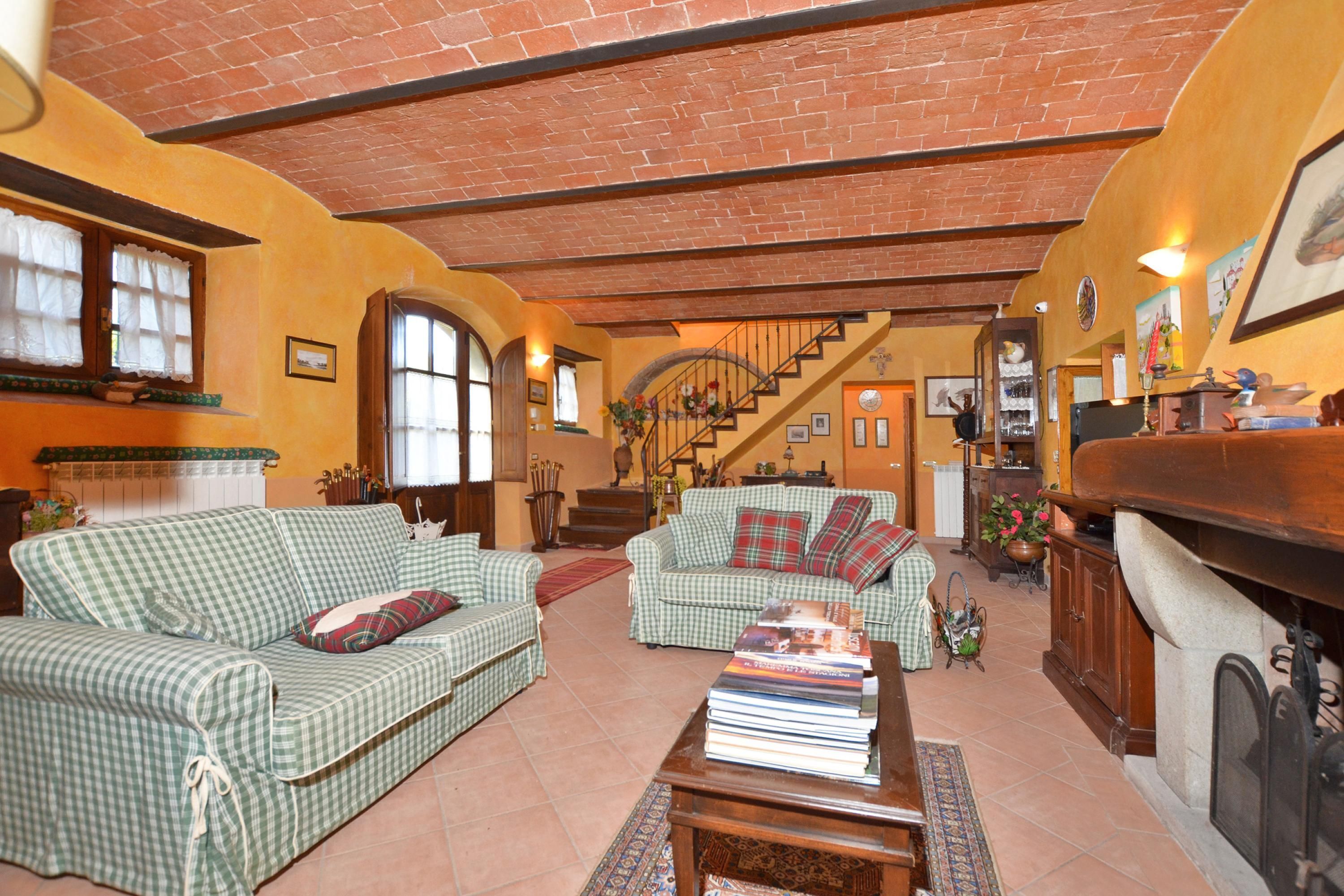 A cozy living room with two green checkered sofas, a fireplace, and a staircase leading to an upper level.
