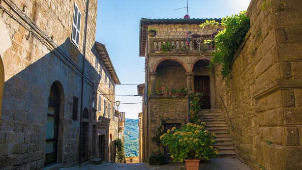 A narrow stone street with a staircase leading to a building with a balcony.