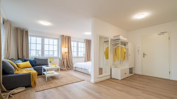 Una habitación de hotel moderna con sofá, cama, armario y vistas al exterior.
