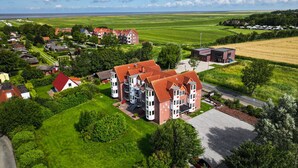 Un edificio grande de varios pisos con techo rojo, rodeado de campos verdes y casas más pequeñas.