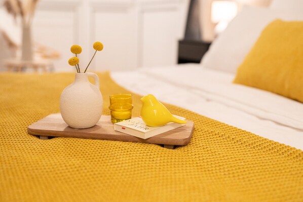 A bed with a yellow pillow, a white vase with yellow flowers, a yellow bird figurine, and a wooden tray with a small book and a yellow bottle. - Hansekogge 2-2 Rental. Romantic with a terrace. (Wurster Nordseeküste)