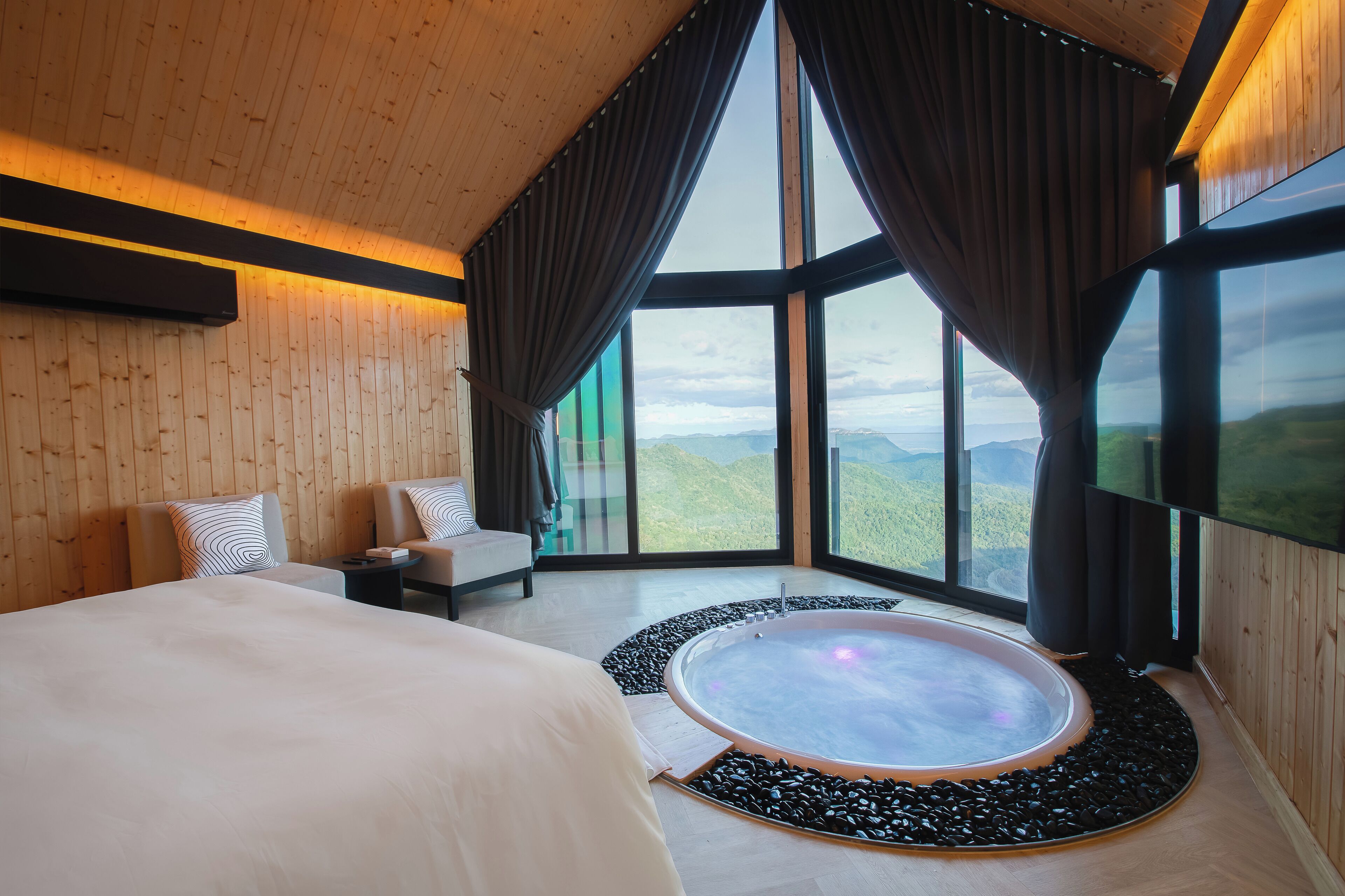 A modern bedroom with a large bed, a sitting area, and a hot tub.