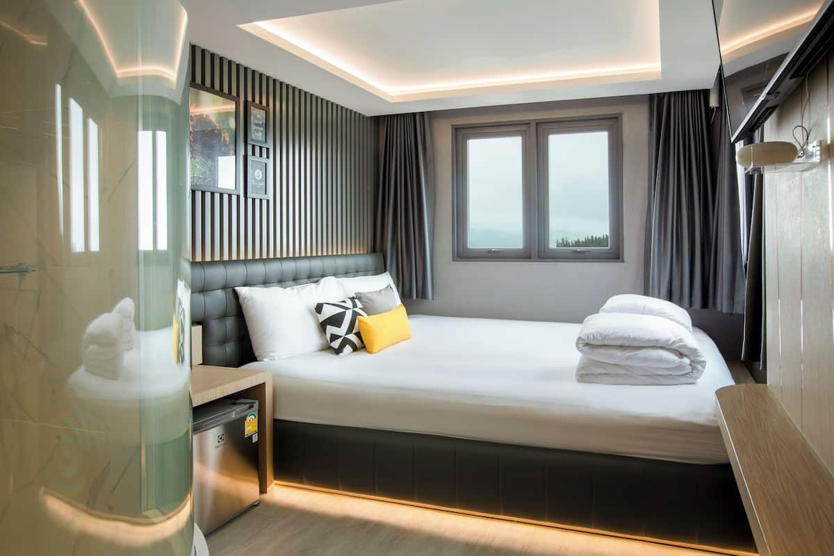 Ein modernes Hotelzimmer mit einem großen Bett, einem Nachttisch, einem integrierten Fernseher und einem Fenster mit Vorhängen.