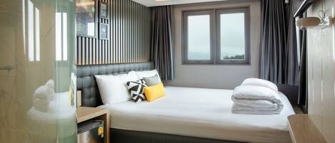 A modern hotel room with a large bed, a bedside table, a built-in TV, and a window with curtains.