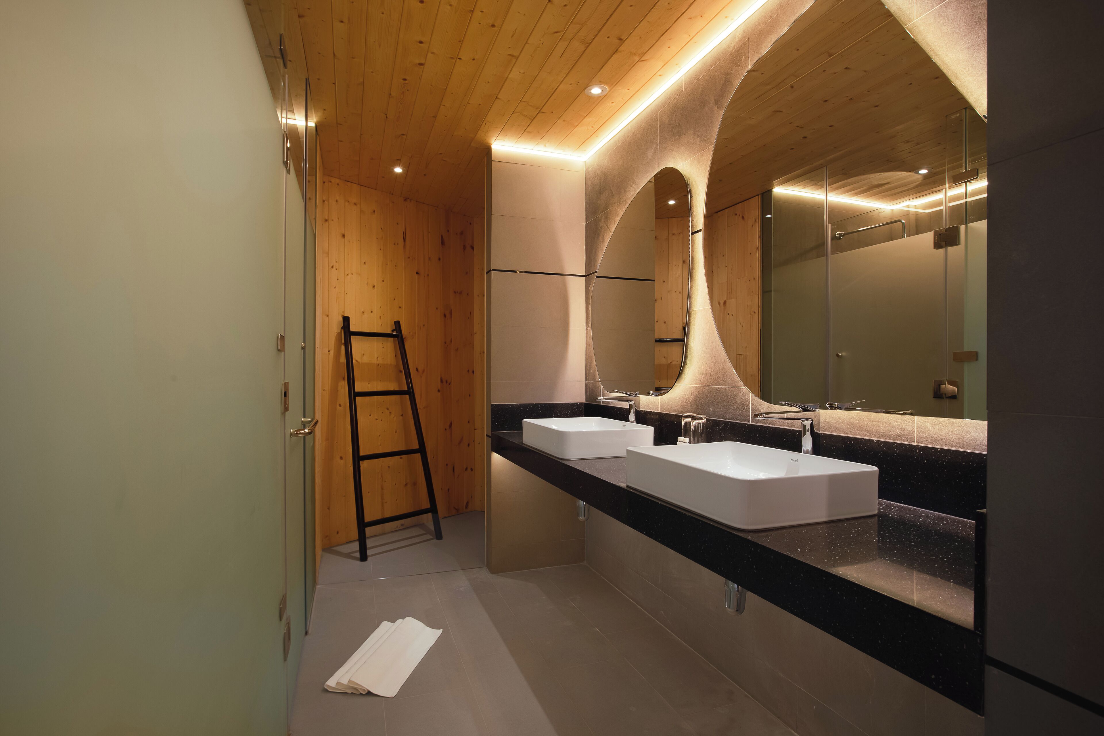 A modern bathroom with wooden ceiling, two sinks, and a large mirror.