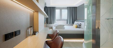 A modern hotel room with a wooden desk, leather chairs, a bed with a view, and a glass shower enclosure.