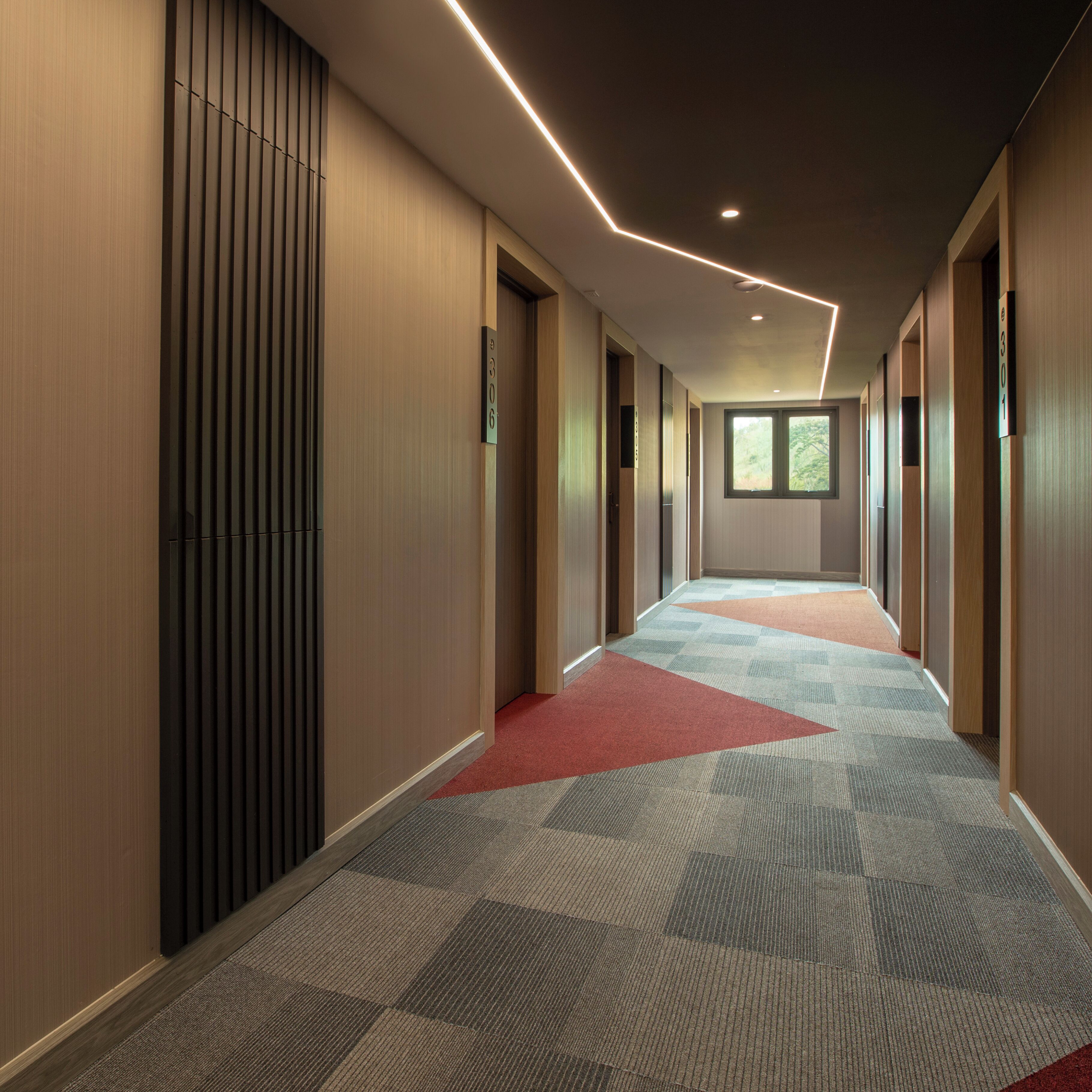 A modern hallway with wooden paneling, a patterned carpet, and a ceiling with recessed lighting.