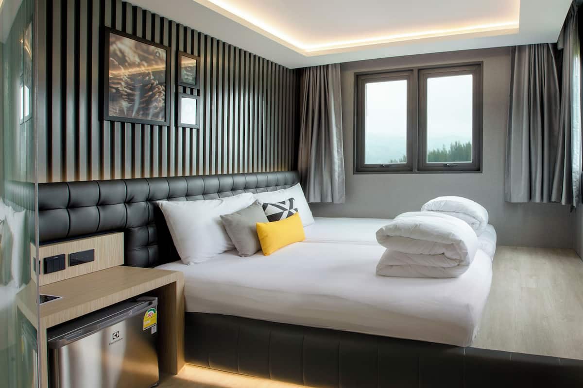Ein modernes Hotelzimmer mit einem großen Bett, einem integrierten Schreibtisch und einem Fenster mit Vorhängen.