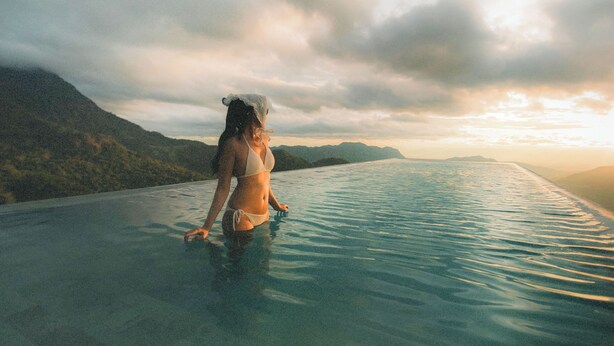 Une personne en bikini, debout dans une piscine à l’eau claire, avec un paysage montagneux en arrière-plan.