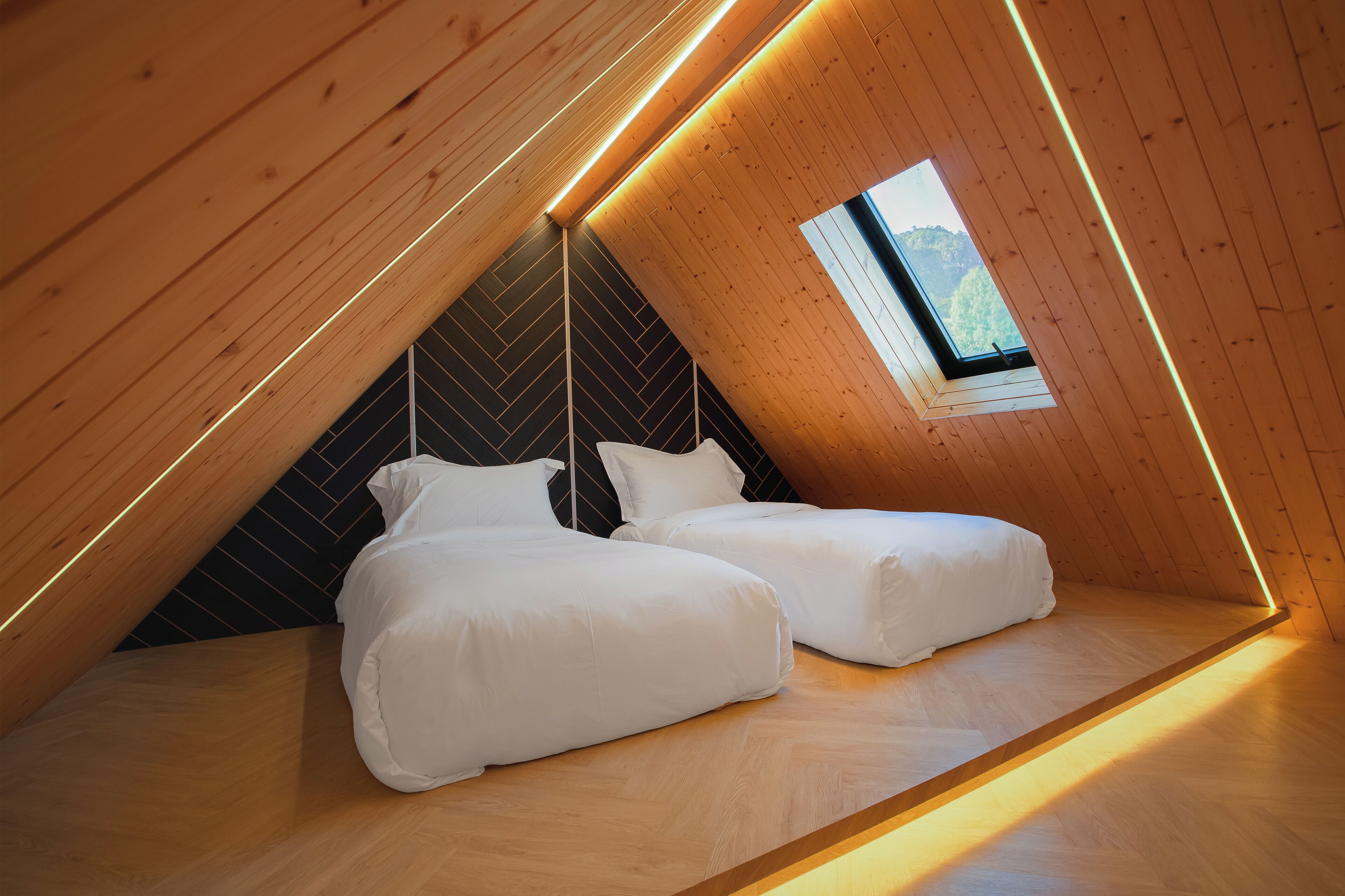 Un dormitorio acogedor en el ático, con dos camas, paredes de madera y un tragaluz.