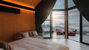 Une chambre moderne avec un grand lit, un canapé et une vue sur les montagnes, visible à travers de grandes fenêtres.