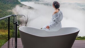 Une personne assise dans une baignoire, d’où elle peut admirer un paysage montagneux enveloppé de brume.