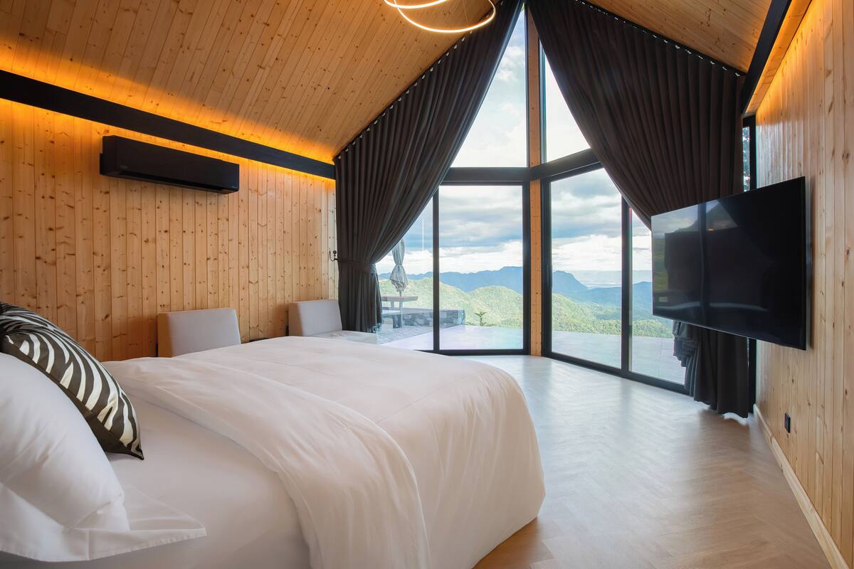 Ein modernes Schlafzimmer mit einem großen Bett, einem Flachbildfernseher und Bergblick durch große Fenster.