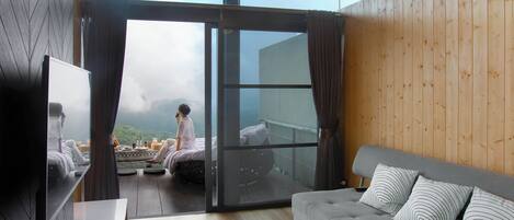A modern living room with a sofa, a flat-screen TV, and a large sliding glass door leading to a balcony.