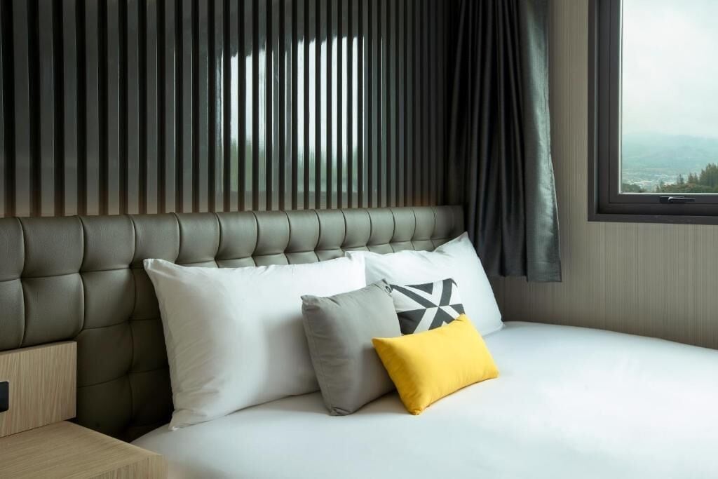 Ett hotellrum med en stoppad sänggavel, en säng med vita sängkläder och ett fönster med utsikt.