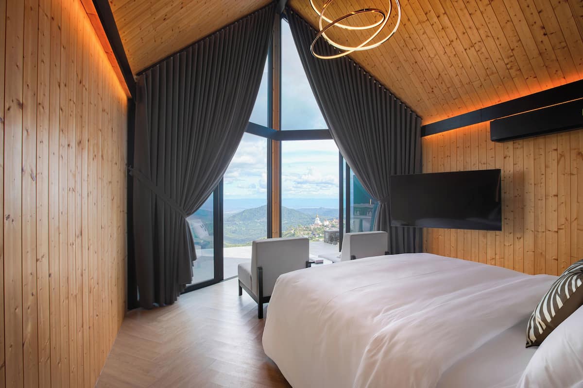 Ein modernes Schlafzimmer mit einem großen Bett, einem an der Wand montierten Fernseher und Bergblick durch große Fenster.