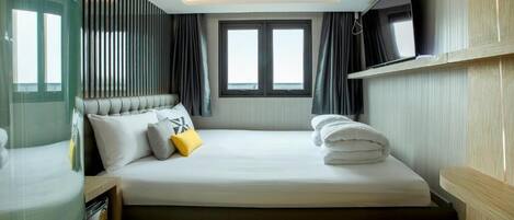 Una habitación de hotel moderna con una cama grande, un televisor de pantalla plana y una ventana con cortinas.