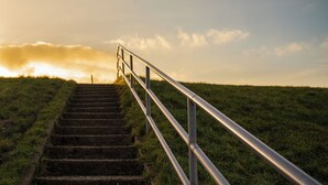 A set of outdoor stairs with metal railings leading up a grassy hill.