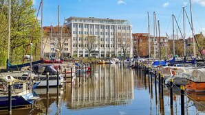 A marina with boats docked, a building with large windows, and a clear sky. - Vacation apartment Moni's Haven. Dream view and loggia. (Bremerhaven)