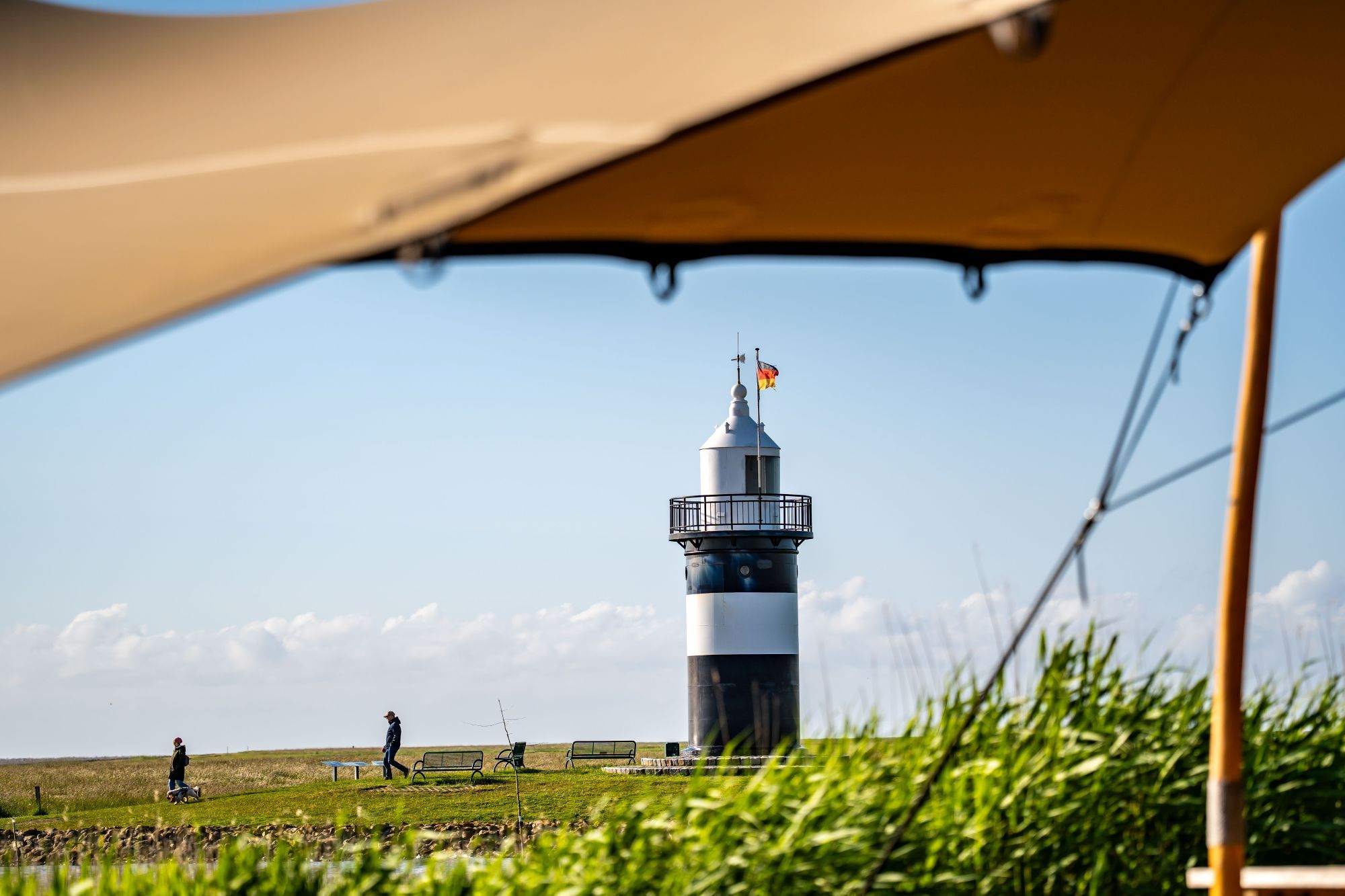 Een vuurtoren met een vlag, een persoon in beweging en een tent op de voorgrond.