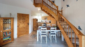 Eine geräumige Küche mit Holzausbau, einem Esstisch mit Stühlen und einer Holztreppe mit Geländer.