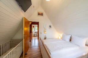 A bedroom with a bed, a wooden staircase, and a view of a kitchen and bathroom. - Vacation home Rotersand 2 - charming and in the middle of the action. (Wurster Nordseeküste)