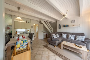 A spacious living area with a sofa, coffee table, and dining table. There is a kitchen in the background with cabinets and a microwave. - Vacation home Rotersand 2 - charming and in the middle of the action. (Wurster Nordseeküste)