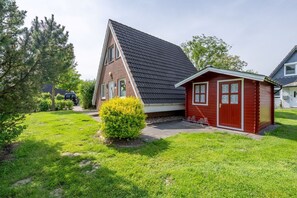 A house with a sloped roof, a small red shed, and a well-maintained lawn. - Vacation home Rotersand 2 - charming and in the middle of the action. (Wurster Nordseeküste)