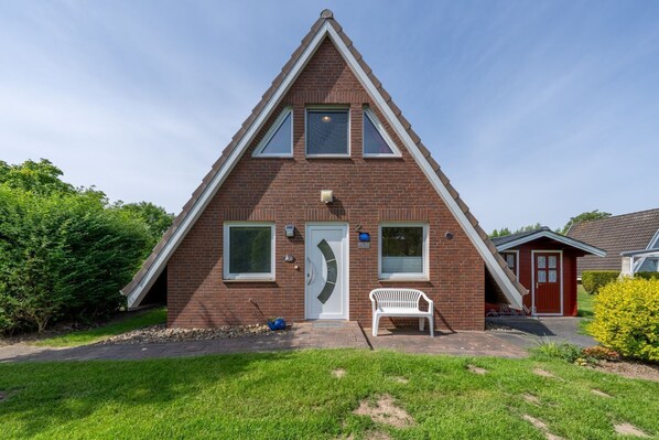A two-story house with a triangular roof, a front door, and a small porch with a bench. - Vacation home Rotersand 2 - charming and in the middle of the action. (Wurster Nordseeküste)