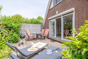A patio with outdoor furniture, a grill, and a badminton set. - Vacation home Rotersand 2 - charming and in the middle of the action. (Wurster Nordseeküste)
