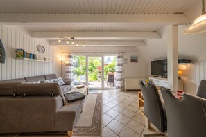 Ein Wohnzimmer mit einer Couch, einem Couchtisch und einem Fernseher. Eine Glastür führt zu einem Außenbereich.