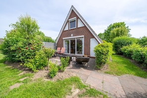 A house with a triangular roof, a patio with chairs, and a garden with various plants. - Vacation home Rotersand 2 - charming and in the middle of the action. (Wurster Nordseeküste)