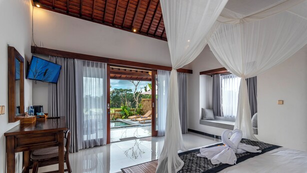 A bedroom with a bed, a desk, a TV, and a view of an outdoor pool.