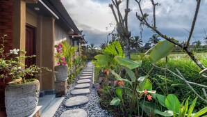 A pathway leading to a house with a tiled roof, surrounded by lush greenery and flowering plants.